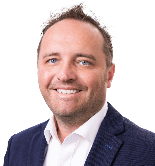 A smiling professional man wearing a dark blazer and a white shirt. He has short, light hair and blue eyes. The background is neutral, focusing on the individual's approachable expression, ideal for representing consultancy expertise.