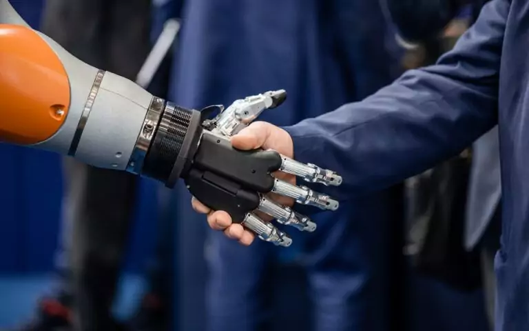 Robot and human hand shaking to symbolize robotics integration in modern industry
