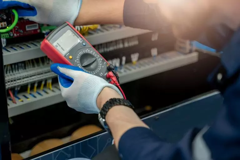 Electrical designer using digital multimeter to inspect electrical panel wiring.