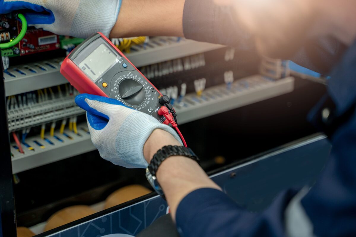Electrical designer using digital multimeter to inspect electrical panel wiring.
