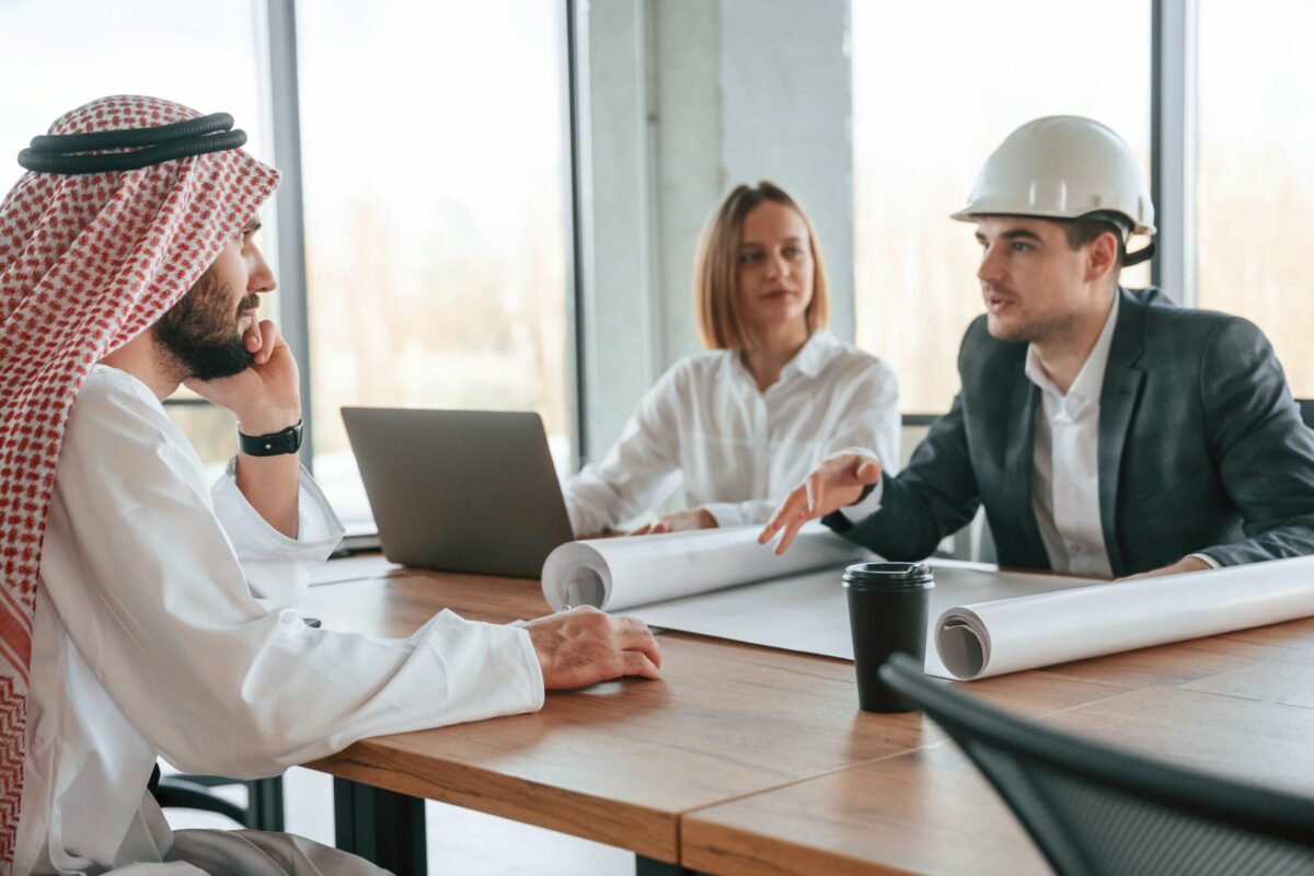 Civil engineer in traditional attire discussing project plans with a team of professionals during an interview in a modern office.