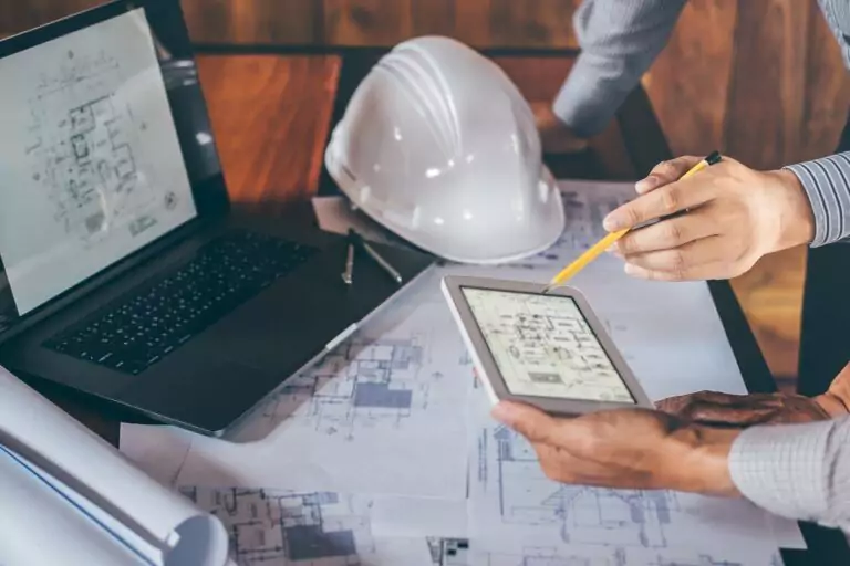 Engineers reviewing building design plans on a tablet and laptop for civil and structural engineering projects.