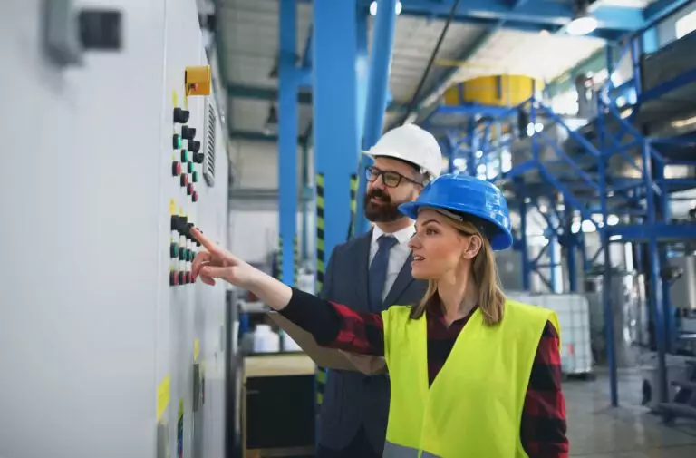 Electrical engineer and technician reviewing industrial control panel to distinguish power systems design from electronics and PLC controls
