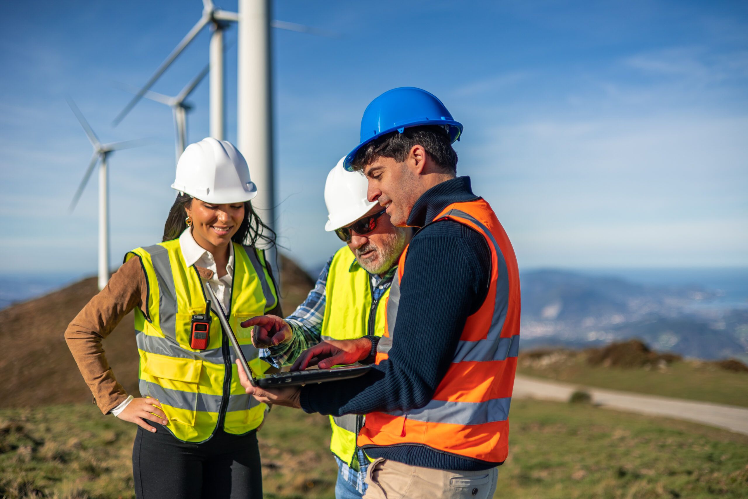 Civil engineers reviewing wind farm site data on a laptop near wind turbines during an energy infrastructure inspection