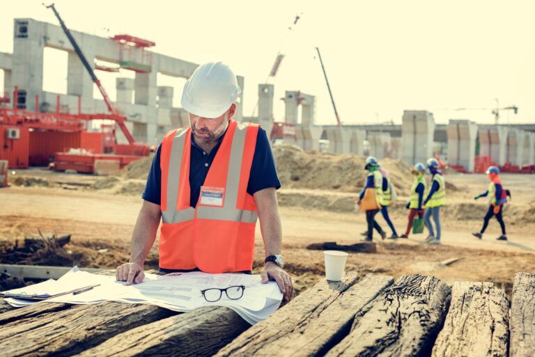 Civil site development engineer reviewing blueprints on an active construction site to manage schedule dependencies and grading plans