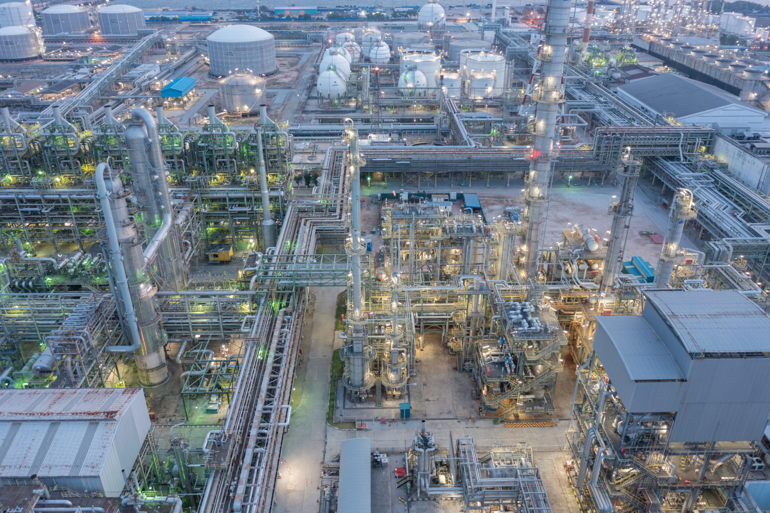 Aerial view of a petrochemical facility with interconnected piping, motors, and heat exchangers at twilight