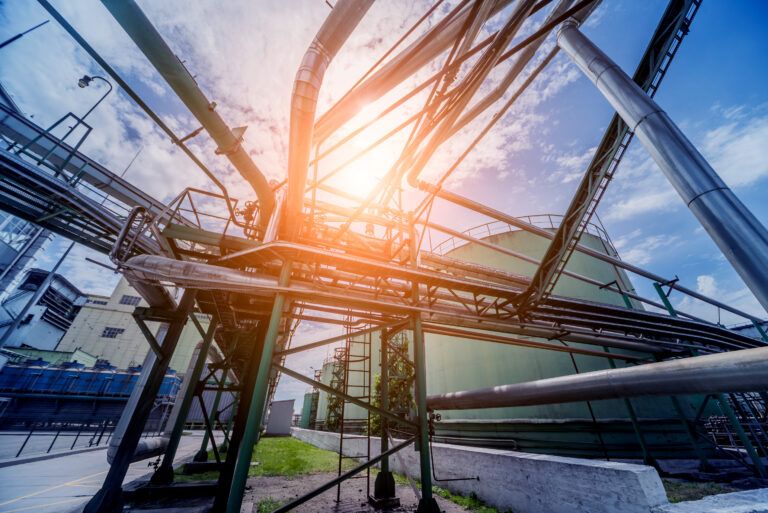 Industrial piping and storage tanks at an oil refinery with sunlight illustrating energy flow and heat integration