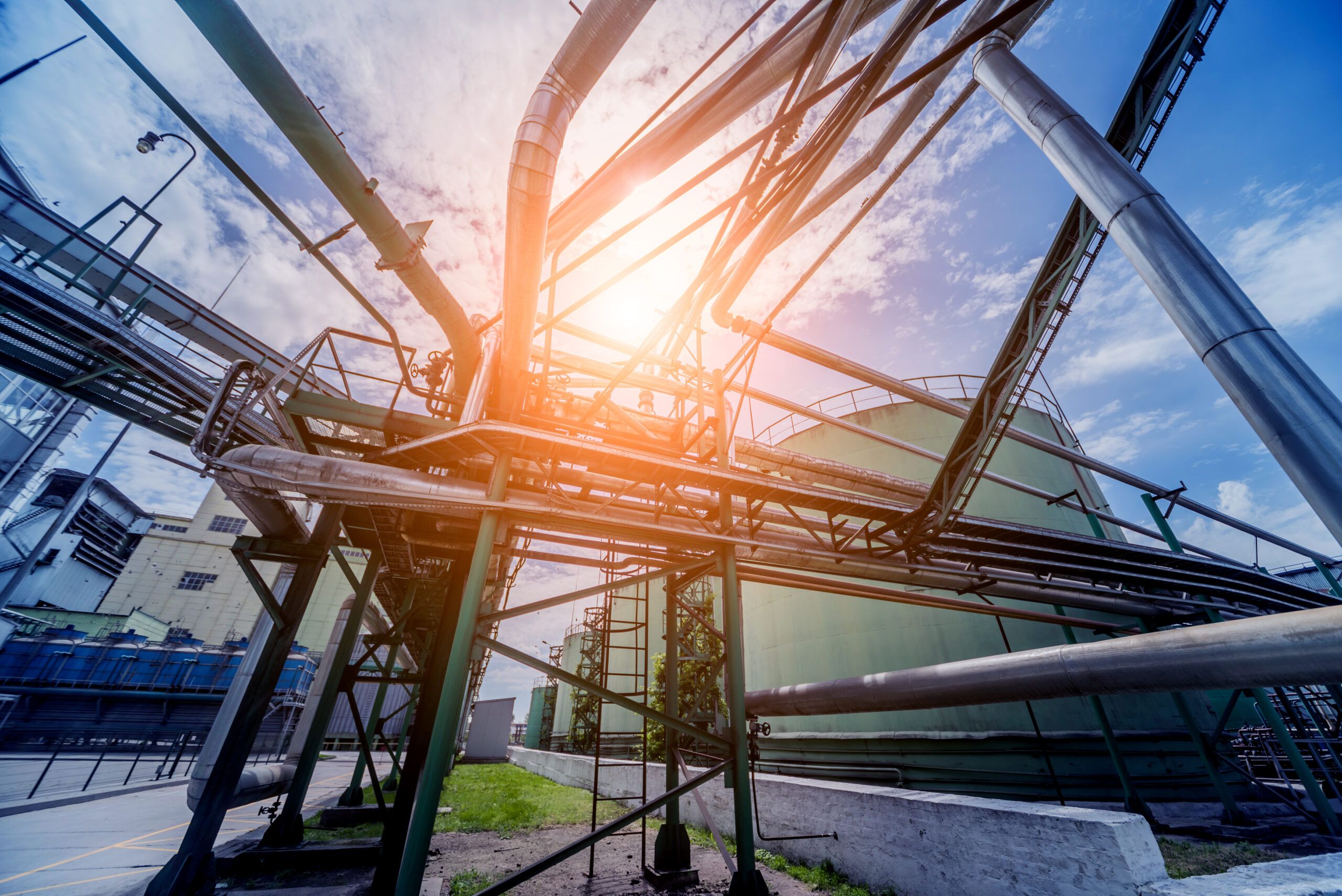Industrial piping and storage tanks at an oil refinery with sunlight illustrating energy flow and heat integration