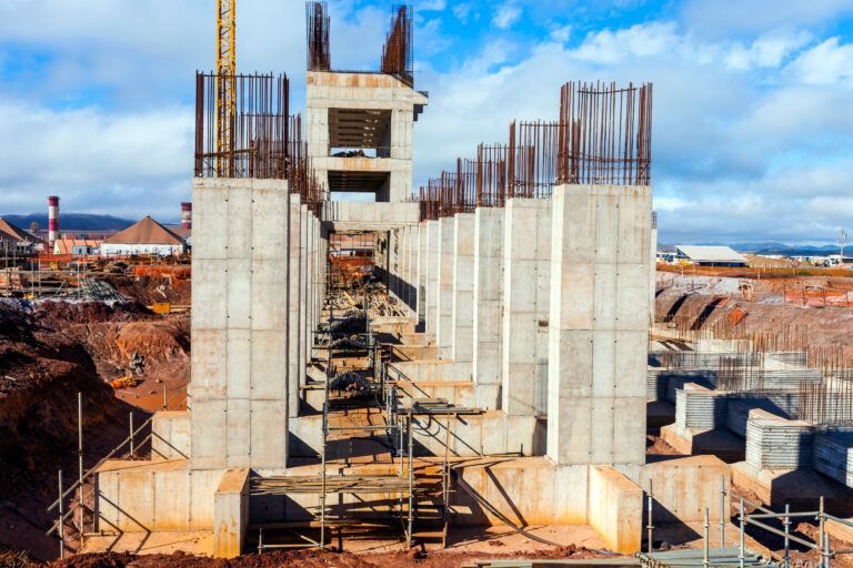 Reinforced concrete foundation columns under construction at a large industrial site with exposed rebar and spread footings