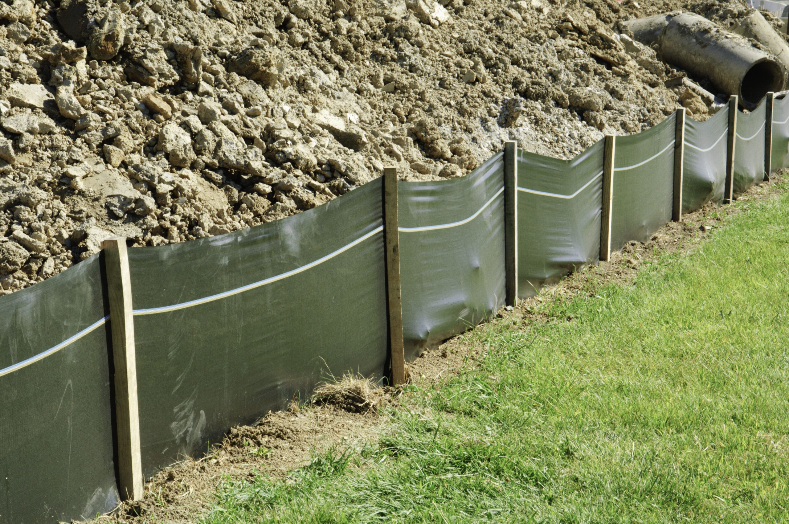 Silt fence with geotextile fabric and wood posts installed along disturbed soil on a construction site