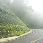 Geosynthetic mesh with anchor plates stabilising a vegetated roadside slope alongside a curved highway in foggy conditions