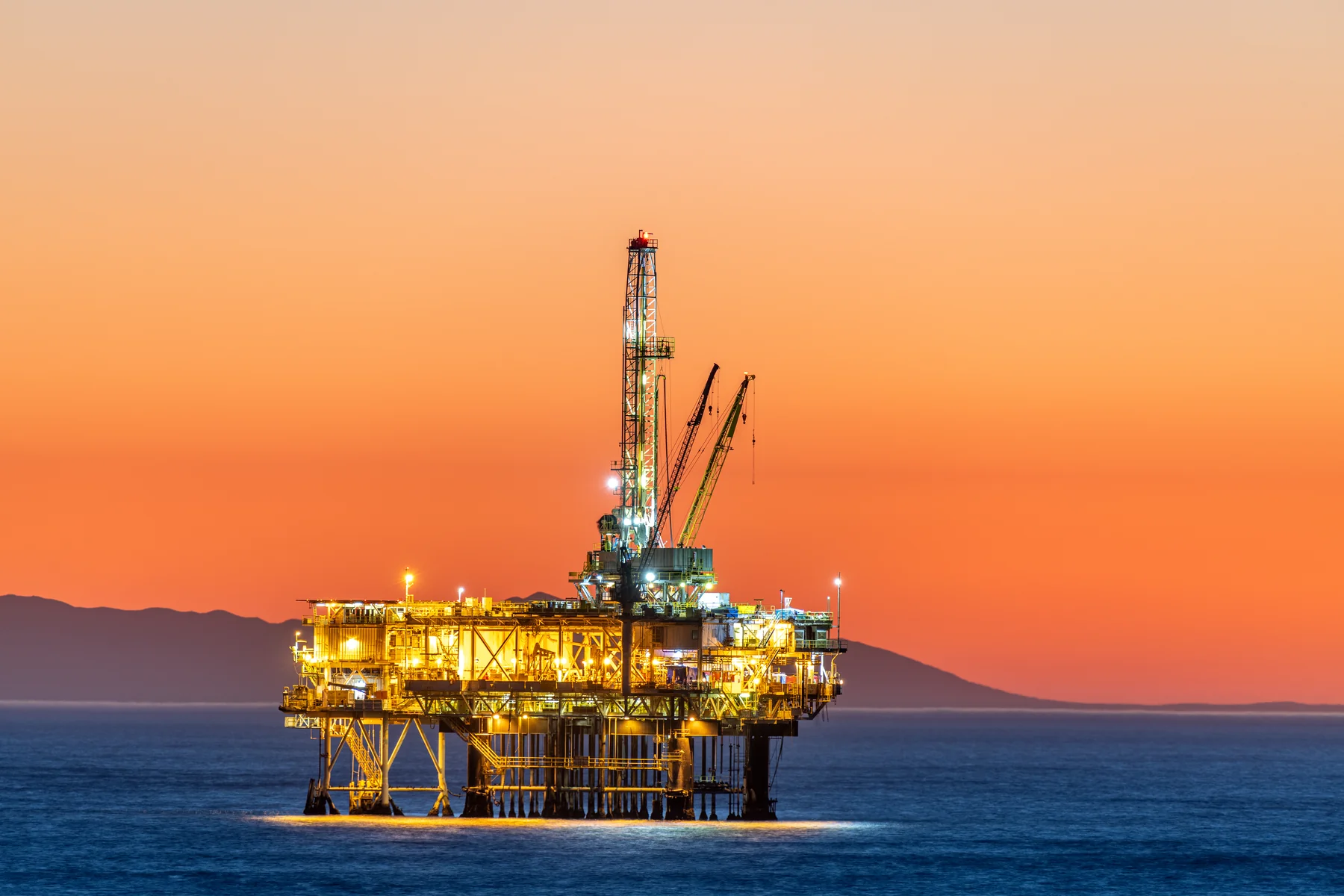 Offshore oil platform illuminated at sunset over ocean